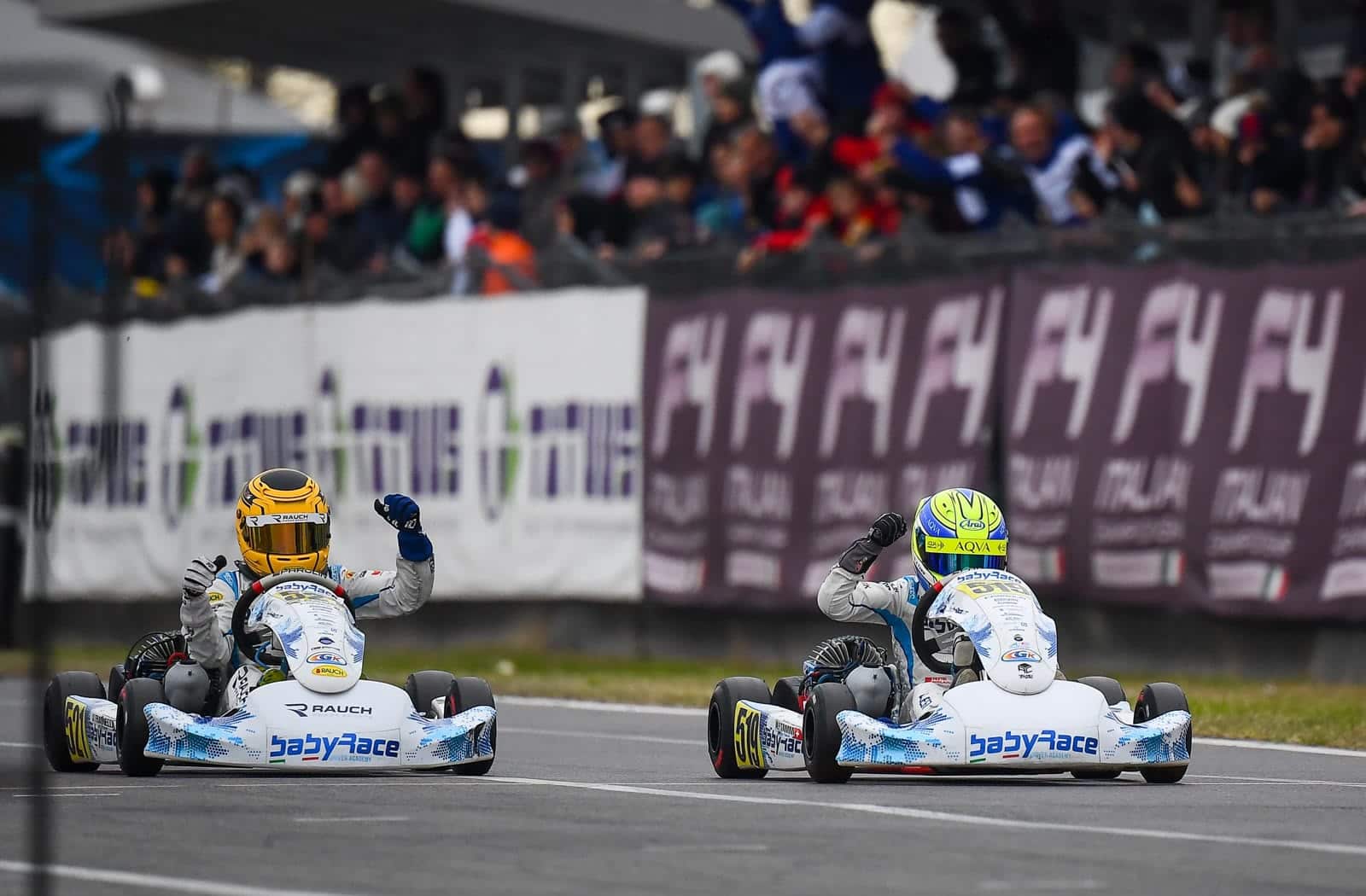 Two BabyRace Driver Academy karts crossing the finish line with their drivers raising a fist in victory