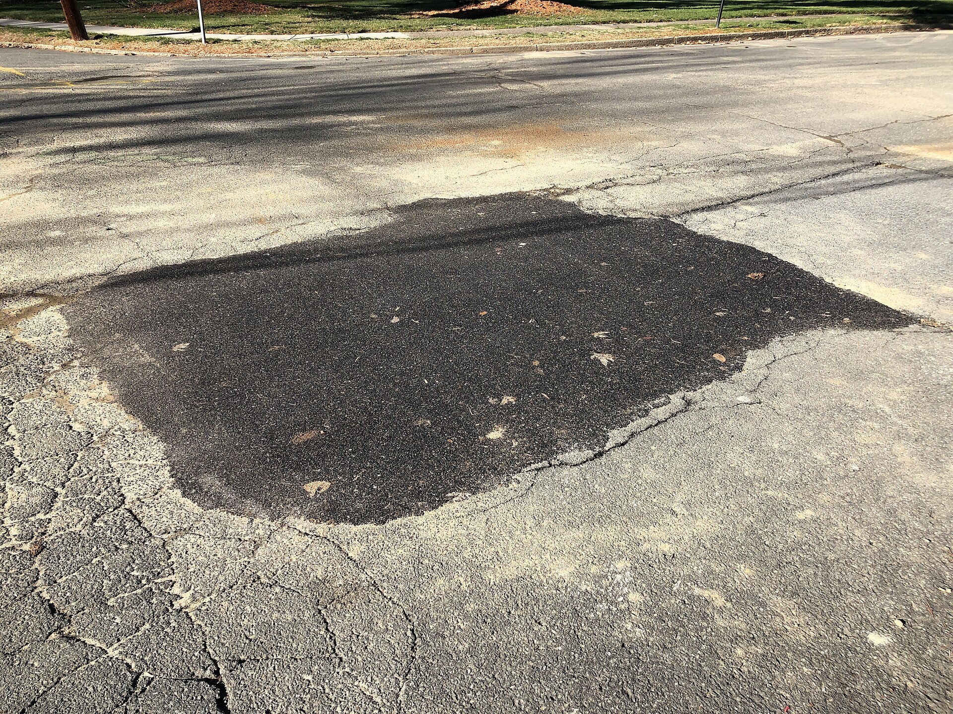 Patched asphalt on a public road showing multiple repair surfaces
