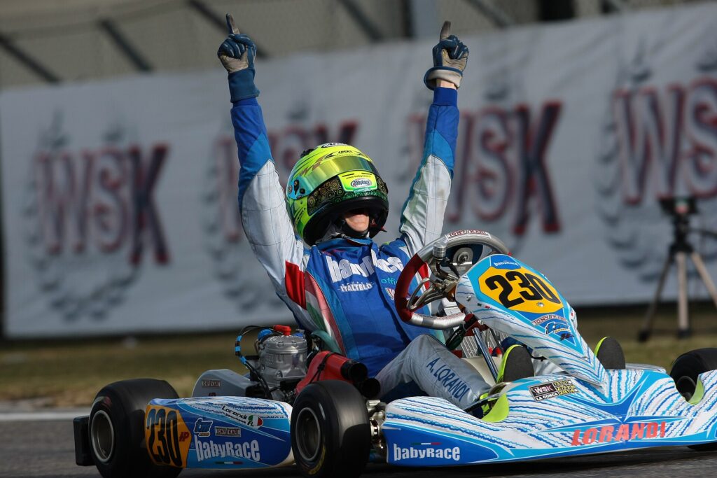 Driver in a blue and white Babyrace-liveried kart, number 230, celebrating a win with both arms raised